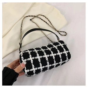 Detailed view of the cylindrical tweed plaid handbag with golden chain strap on fabric