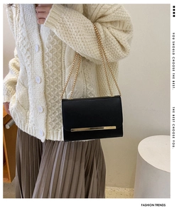 Detail of black envelope crossbody bag with gold metal bar and thin chain straps
