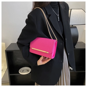 Detalle del bolso de cadena rosa con adorno dorado sobre una chaqueta negra de mujer