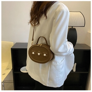 Gros plan d'un mini sac ovale en cuir PU marron avec détails de boutons floraux blancs