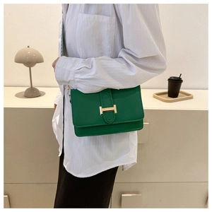Sac bandoulière en cuir vert avec fermoir H doré et sangle à motifs porté par modèle