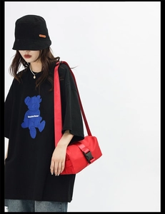 Street style outfit detail featuring a red nylon crossbody bag and bear graphic t-shirt