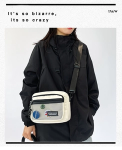 Detail view of beige canvas crossbody bag with black zipper and fashion round badge