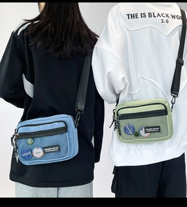 Detail of blue and green street style canvas crossbody bags with front mesh pocket and badges