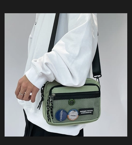 Detail view of green canvas messenger bag with mesh pocket, badges and adjustable strap