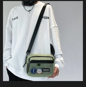Detail view of light green canvas crossbody bag featuring front mesh pocket and logo patch