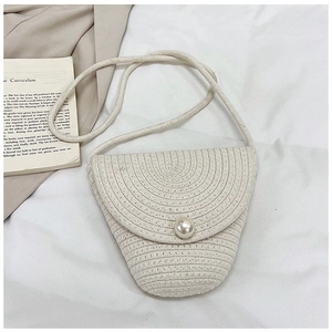 Détail d'un sac bandoulière en paille tissée blanc cassé avec un fermoir bouton perle