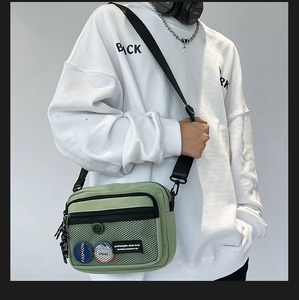 Detail of light green canvas crossbody bag featuring mesh pocket and colorful badges