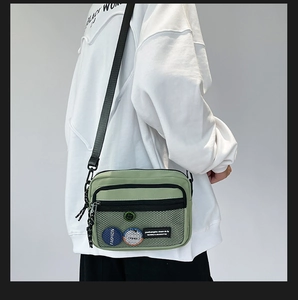 Detail view of grass green canvas crossbody bag featuring front mesh pocket and fashion badge