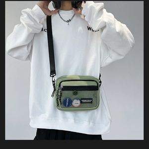 Detail of light green canvas crossbody bag with mesh pocket and fashion badge