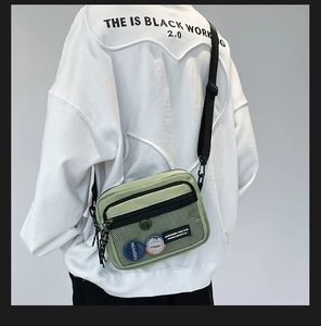 Detail of green canvas messenger bag featuring a mesh pocket and fashion badges