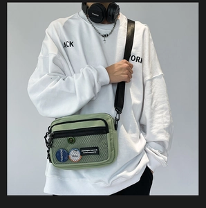 Detail of light green nylon messenger bag with mesh pocket and fashion badges