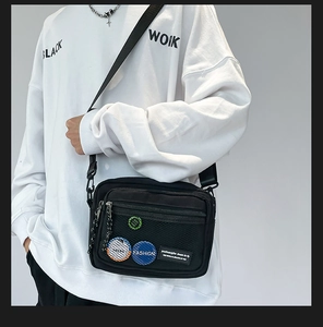 Detail view of black canvas crossbody bag with mesh pocket and trendy fashion badges