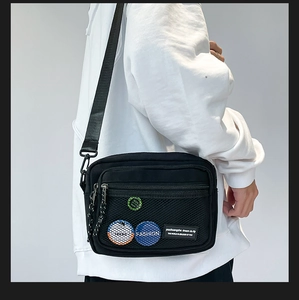 Close-up of black nylon crossbody bag with mesh pocket and colorful badges worn by model