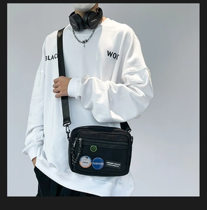 Detail of a black canvas crossbody bag featuring fashion badges and mesh zipper pocket
