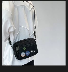 Detail of black canvas messenger bag featuring a mesh pocket with colorful fashion badges