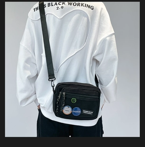 Detailed view of the black canvas crossbody bag with mesh pocket and colorful badges