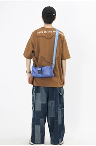 Rear view of a blue oxford crossbody bag with buckle closure worn by a model