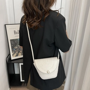 Détail du sac à bandoulière tissé blanc avec une grande perle décorative sur le rabat