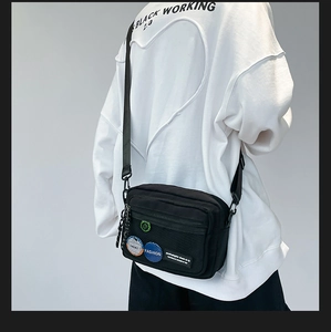 Detail of black canvas crossbody bag featuring mesh pocket and decorative badges