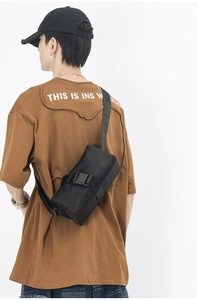 Detail of a black nylon crossbody bag with a large plastic buckle worn on model back