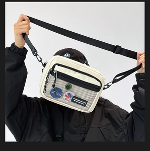 Detail of white canvas messenger bag featuring black mesh pocket and decorative badges