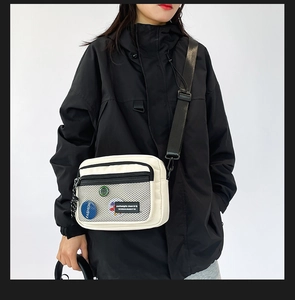Detail of a cream canvas crossbody bag with black mesh pocket and fashion badge