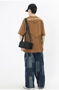 Rear view of brown streetwear t-shirt and blue patchwork jeans with black nylon crossbody bag
