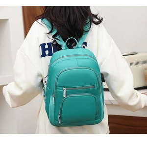 Close-up of turquoise waterproof nylon backpack with multiple zipper pockets on model