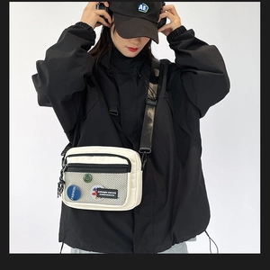 Detail of off-white canvas messenger bag with mesh pocket and fashion badge