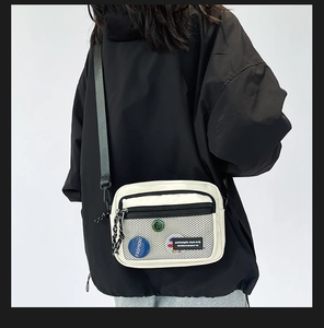 Detail of white canvas crossbody bag with mesh pocket and colorful decorative badges