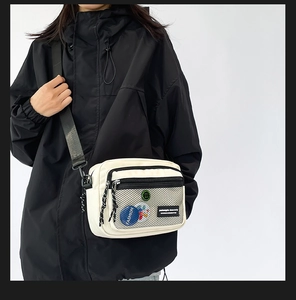 Macro detail of canvas messenger bag featuring a black mesh pocket and fashion badges