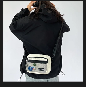Detail of off-white canvas crossbody bag with mesh pocket and colorful cartoon badges