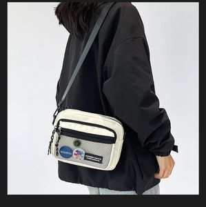 Detail of off-white canvas crossbody bag featuring mesh pocket and colorful badges