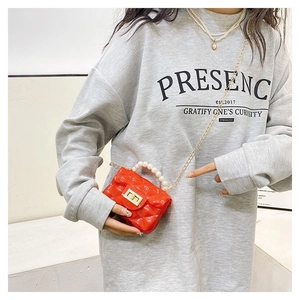 Detailed view of red mini jelly bag with pearl handle and golden chain on a model