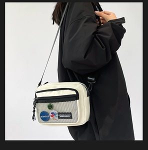Detail of canvas messenger bag featuring mesh pocket and decorative patches on model