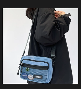 Detail view of light blue canvas crossbody bag with mesh pocket and fashion patches