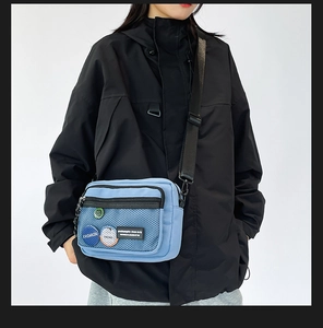 Close-up of blue messenger bag featuring mesh pocket and three decorative badges