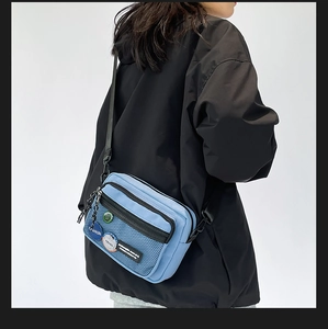 Detail of blue canvas messenger bag featuring black mesh pocket and fashion badges