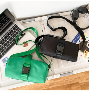 Detail of minimalist cylinder crossbody bags with large tactical buckles on a white box