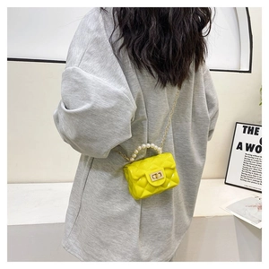 Detail of yellow mini quilted bag with pearl handle and golden chain on a model