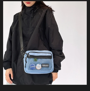 Detail of light blue nylon messenger bag with mesh pocket and fashion pin accessories