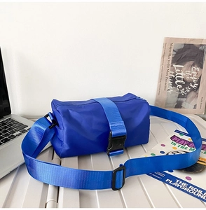 Blue Oxford nylon barrel bag with adjustable strap on a white desk with laptop
