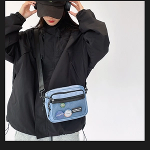 Detail of blue canvas crossbody bag with black mesh pocket and fashion badge decoration