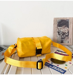 Detail of a yellow nylon crossbody bag with wide adjustable shoulder strap and plastic buckle