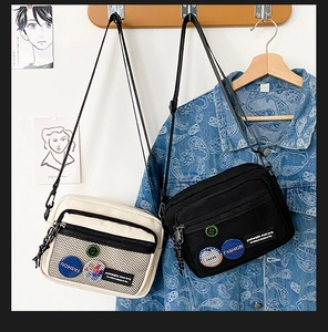 Detail of canvas messenger bags with mesh pocket and fashion patch in black and beige