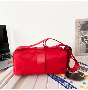 Top view of red nylon crossbody bag with wide strap on a white workspace desk