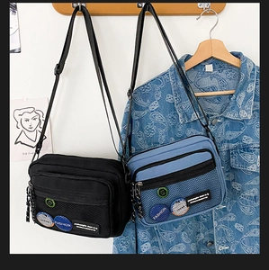 Detail of canvas messenger bags in black and blue with mesh front pocket and badges