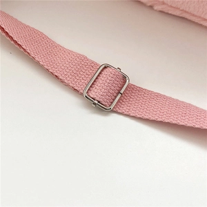 Detalle de la hebilla metálica plateada y la correa tejida rosa del bolso de peluche