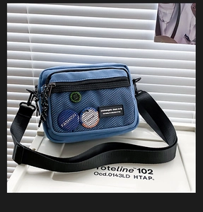 Detail of light blue canvas crossbody bag with mesh pocket and stylish brand badges